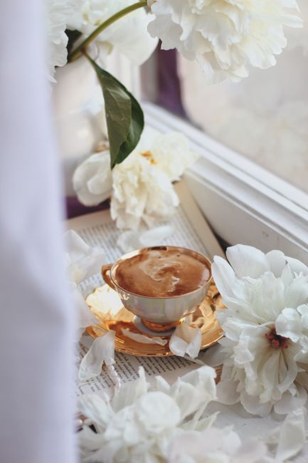 Charming scene of coffee cup amidst blooming white peonies on a soft-lit windowsill.