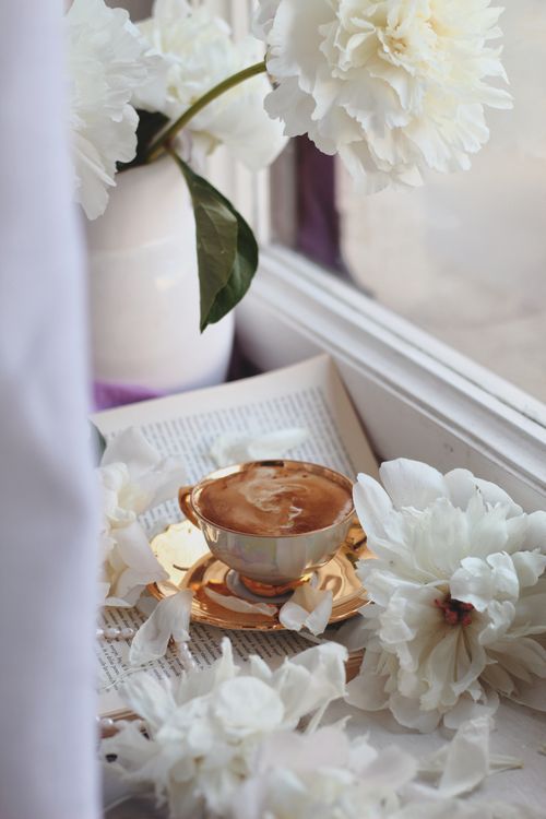 Free A gold-rimmed cup of coffee surrounded by blooming white peonies near a window offers a peaceful, elegant setting. Stock Photo