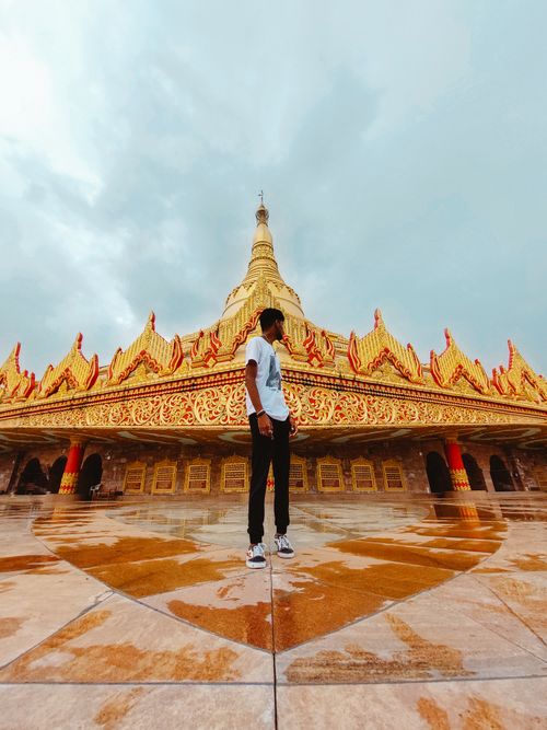 Free Man standing before a grand temple with intricate golden architecture under an overcast sky. Stock Photo