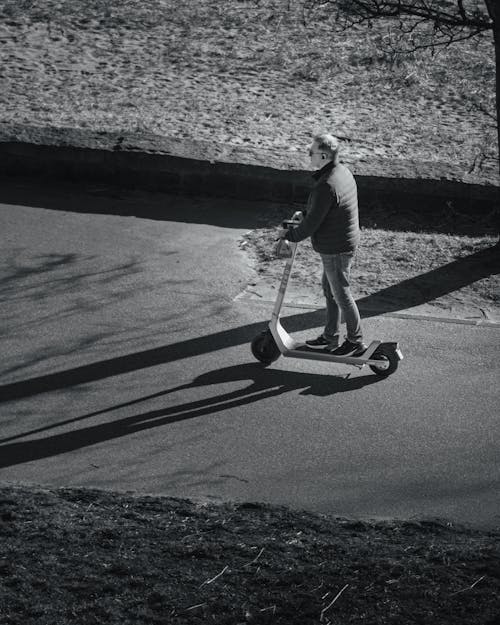 Grayscale Photo of a Man Riding an Electric Scooter