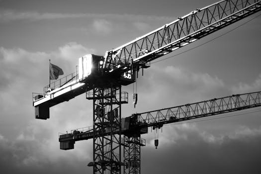 Black and white image of a tower crane with dramatic clouds backdropping the construction site.