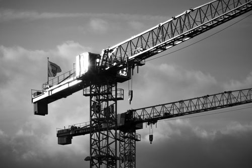 Free Black and white image of a tower crane with dramatic clouds backdropping the construction site. Stock Photo
