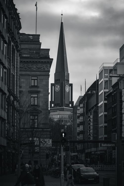 Free Black and white image of a gothic church tower amidst city buildings. Low angle, dramatic mood. Stock Photo