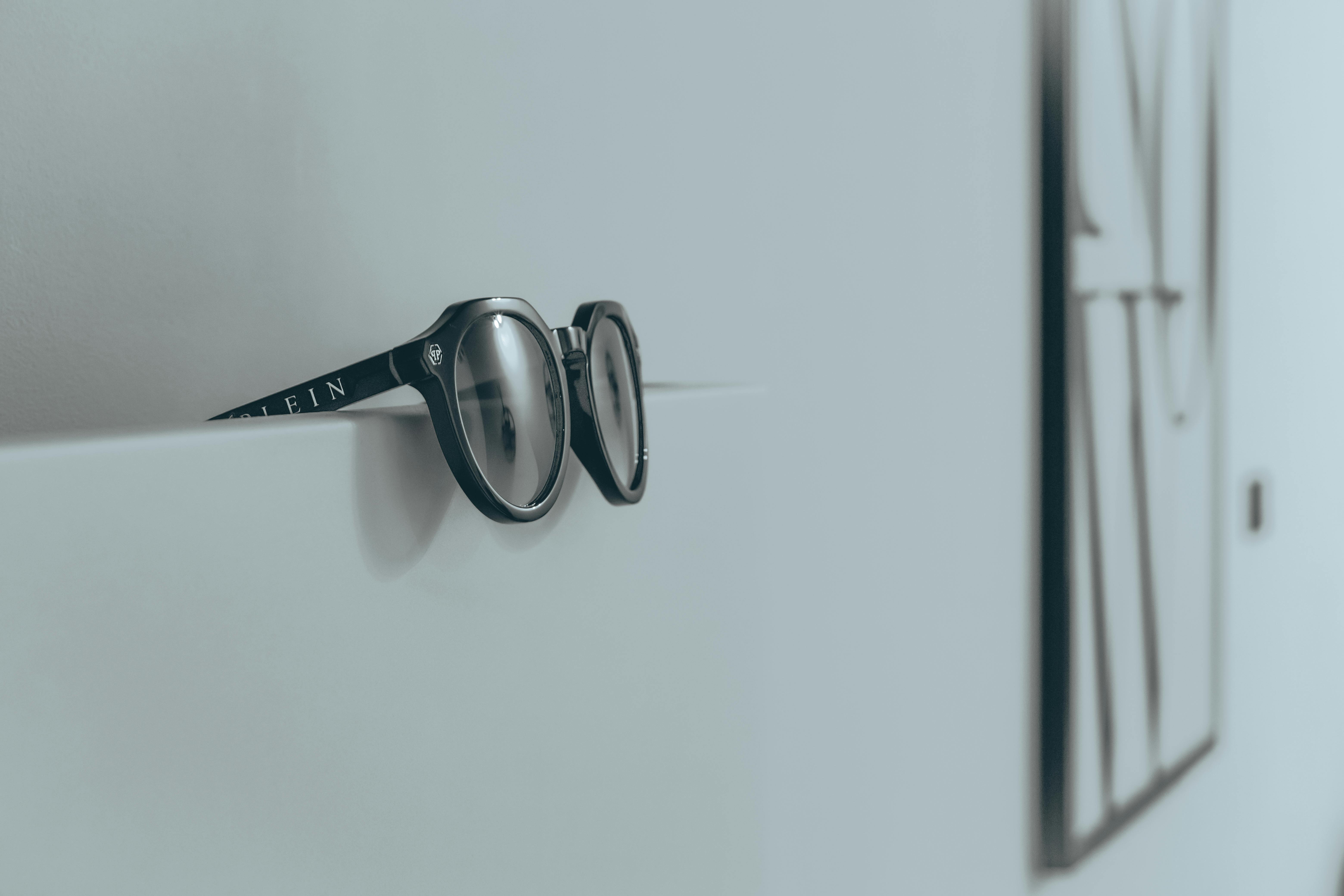Close-up of black sunglasses resting on a minimalist white wall, fashion-focused decor.