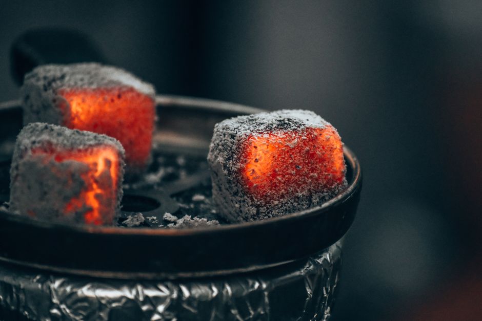 Close-up of glowing charcoal cubes on a metal plate, showing natural coconut coals used for hookah