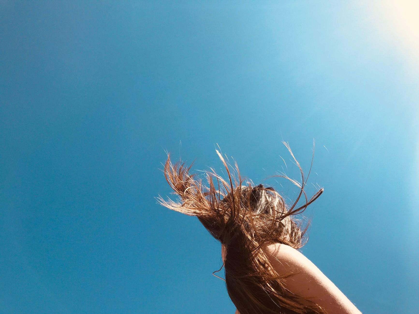 A woman with flowing hair in the bright sunlight and clear blue sky.