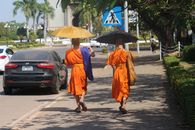 Two Buddhist monks walking on a sunny sidewalk in Vientiane, Laos with umbrellas for shade.