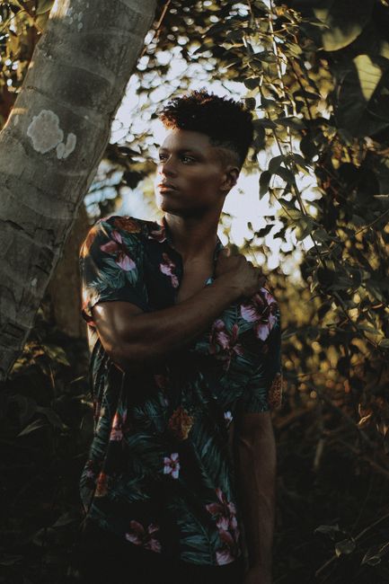 Fashionable young man posing amidst lush tropical foliage with a contemplative look.