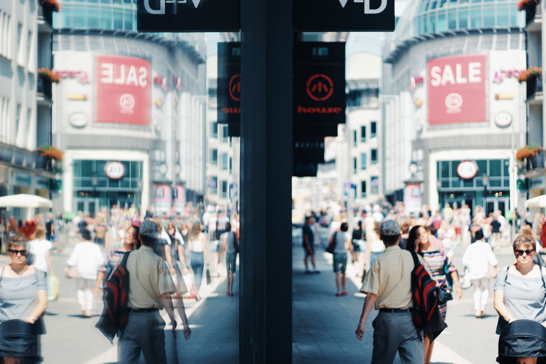 Crowded urban shopping street with mirrored reflections, SALE signs, and diverse pedestrians.