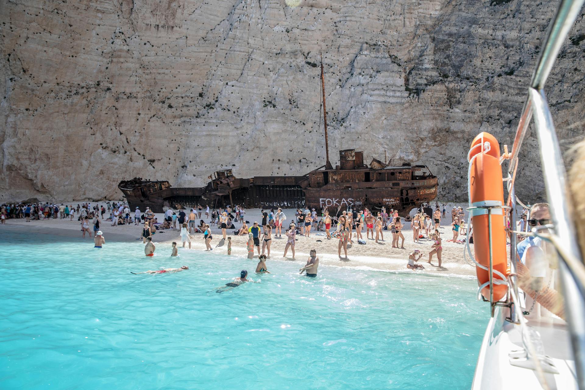 A vibrant summer scene at Navagio Beach, showcasing the famous shipwreck and tourists enjoying the clear waters in Greece.