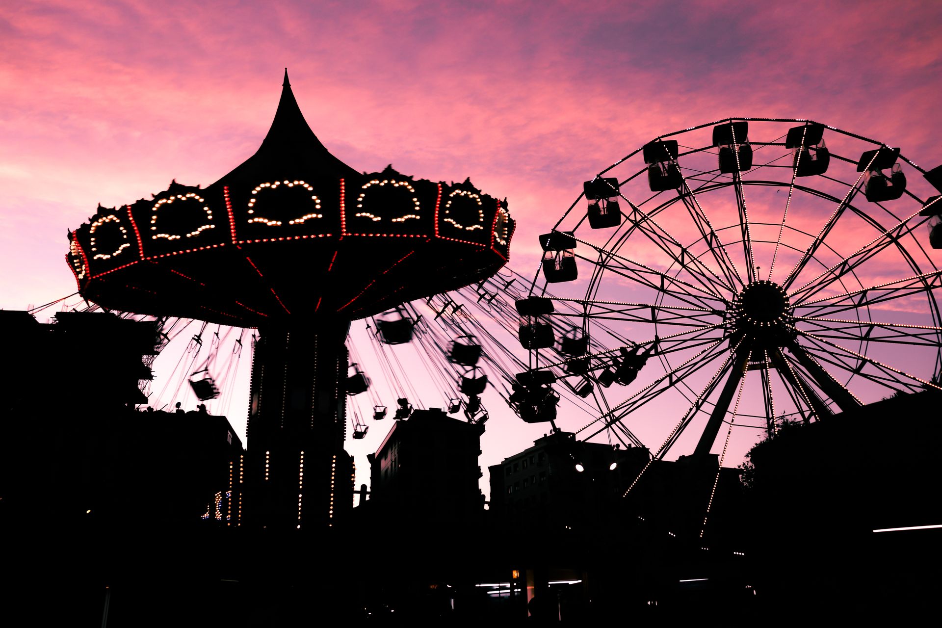 Amusement park rides silhouetted against a vibrant twilight sky with a ferris wheel and swing ride.