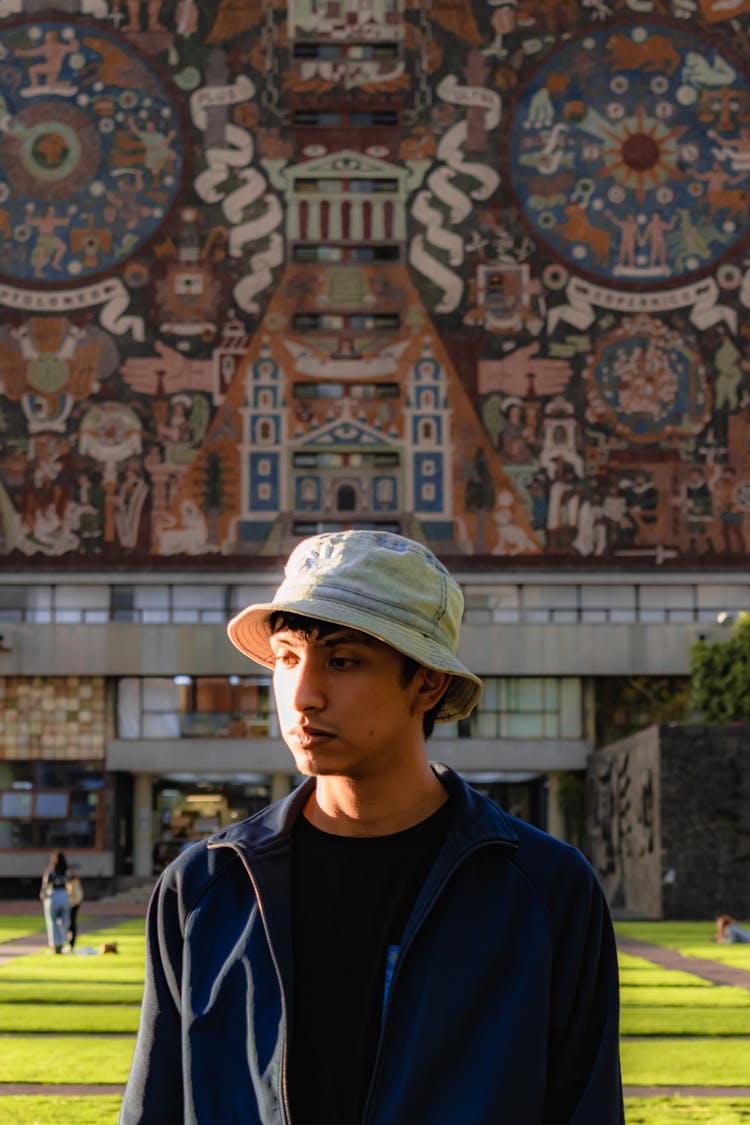 Photo Of A Young Man Against The Background Of The Building Of The National Autonomous University Of Mexico