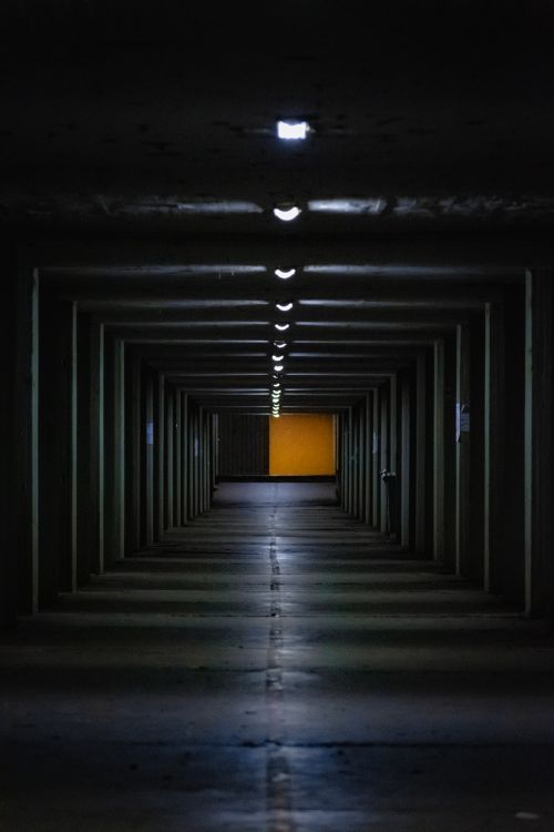 Free A dark, moody hallway in an industrial building, lit by a series of overhead lights. Stock Photo