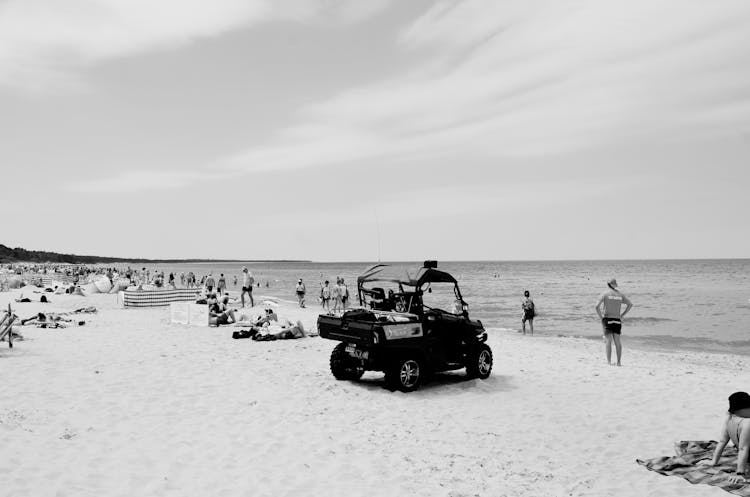 Black And White Photo Of People And A Rescue Services Car On A Beach