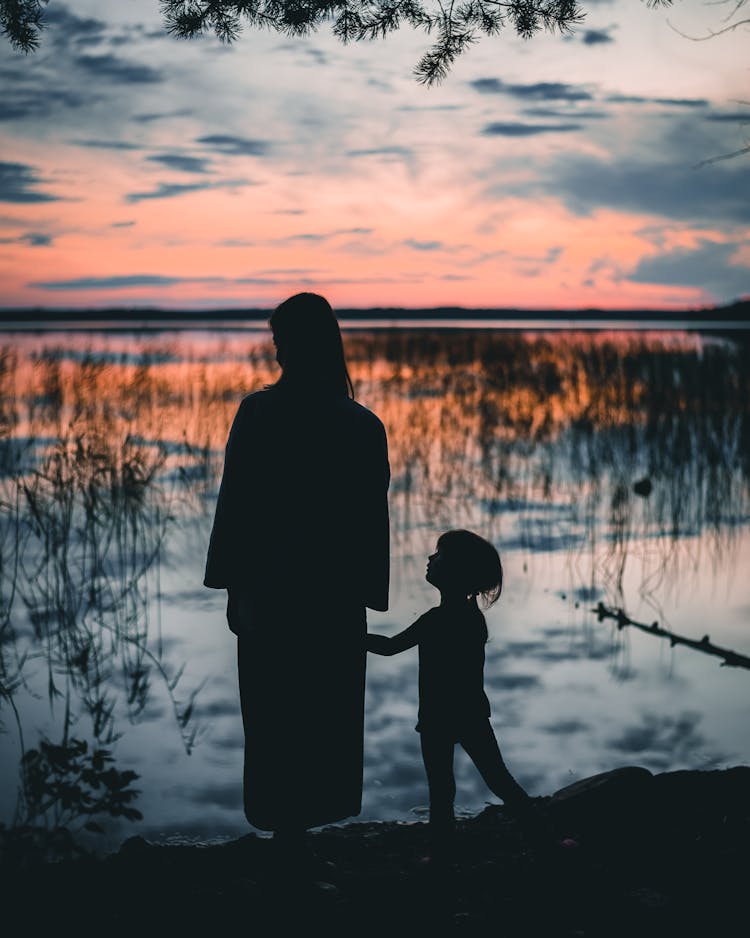 Silhouette Of Mother And Child Standing Beside The Lake