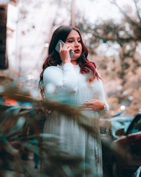 A young woman in a white dress using her smartphone outdoors on a sunny day.