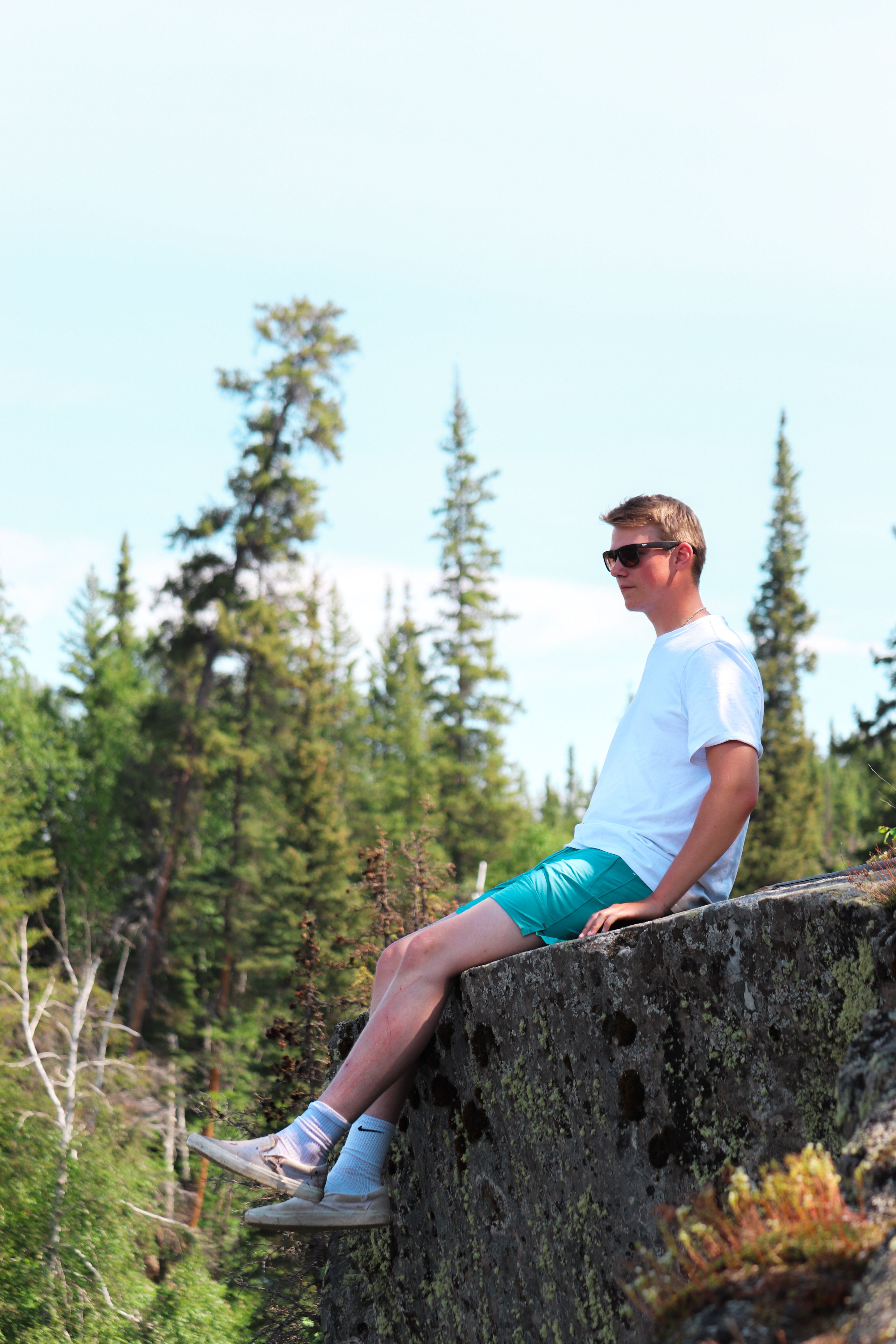 A young man sits on a forest rock formation, enjoying a sunny day.