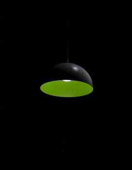 Stylish black pendant lamp with vivid green interior against dark background for dramatic effect.