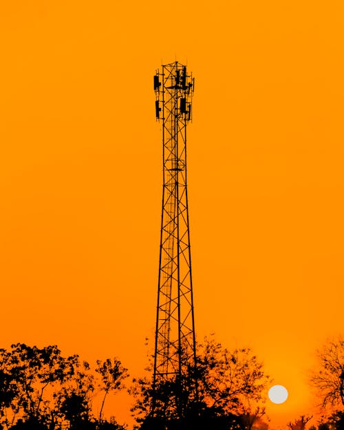 Silhouette of Communication Tower Near Green Trees Under Golden Sky