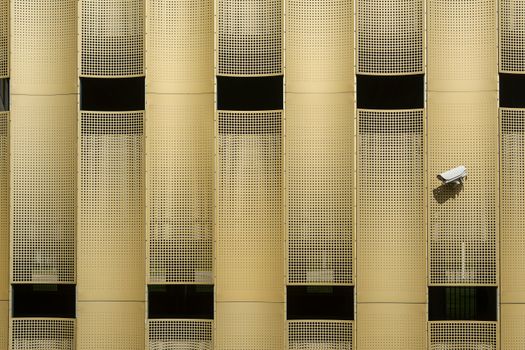 Close-up of a modern building facade with a prominent CCTV camera, showcasing architectural design.