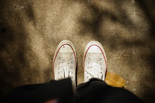 Free Top view of worn white sneakers on sunlit concrete ground with leaf. Stock Photo