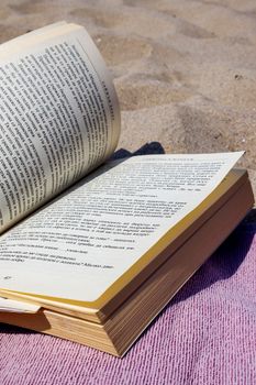 An open book rests on a blanket on a sunny beach, offering a relaxing scene.
