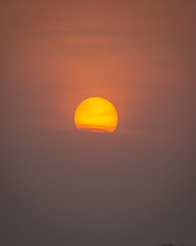 A vibrant sunset with a radiant sun partially obscured by haze in Sillanwali, Punjab.