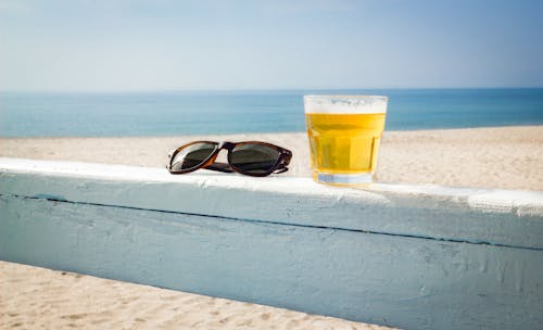 A Glass of Beer and a Pair of Sunglasses on a Wooden Railing