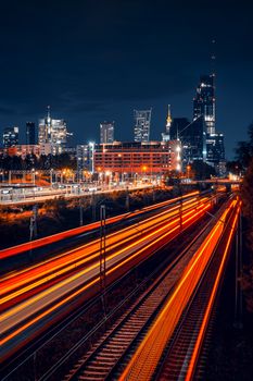 Dynamic night view of Warsaw skyline with vibrant train light trails creating motion effect.