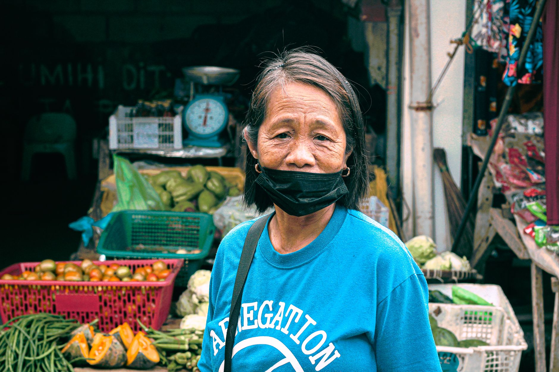 A rural Philippine market with a smartphone displaying a cockfight video, spectators blurred behind the screen