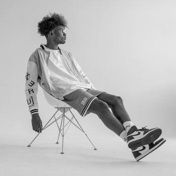 Stylish black and white portrait of a man sitting in a modern chair in a studio setting.