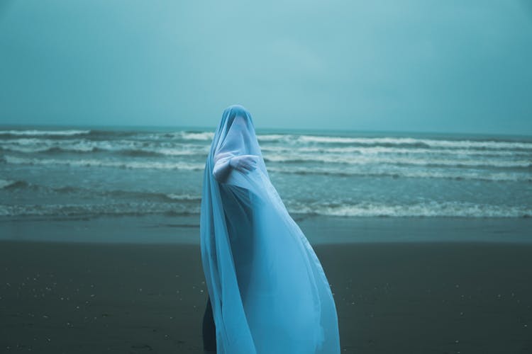 Person Covered With White Cloth Standing On Beach