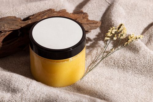Free Jar of yellow skincare cream on a towel with wood and dried flowers, ideal for spa themes. Stock Photo
