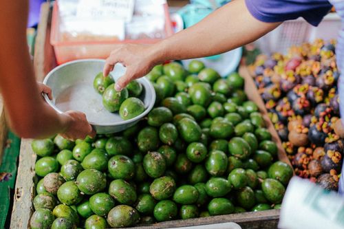 Free Fresh green mangoes being selected at a bustling outdoor fruit market stand. Stock Photo
