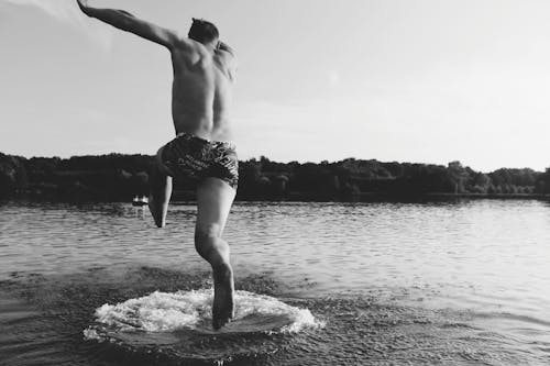 Grayscale Photography Of Man Jumping On Body Of Water