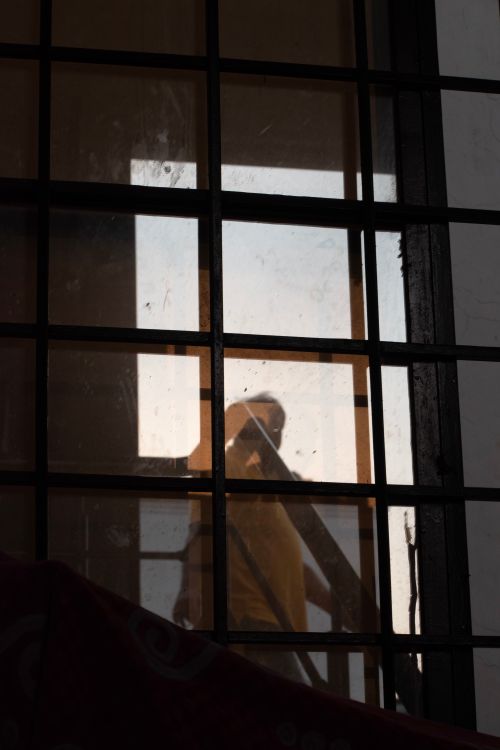 Free A mysterious silhouette of a person seen through a glass window grid during evening light. Stock Photo
