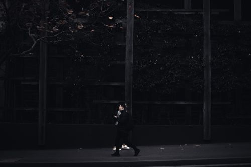 Free A solitary figure walks along a dimly lit urban street, capturing a moody city atmosphere. Stock Photo
