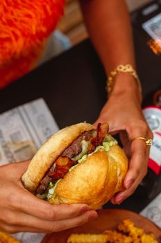 Close-up view of a gourmet burger with bacon held by unrecognizable person, emphasizing savory and fresh ingredients.