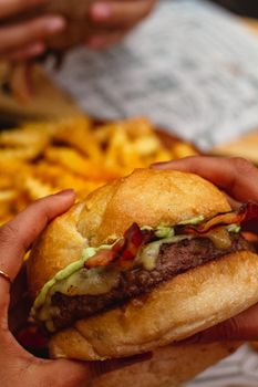 Delicious homemade burger with melted cheese and fries in the background, perfect for fast food lovers.