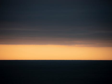 Moody sunset with dark clouds over ocean horizon, perfect for backgrounds.