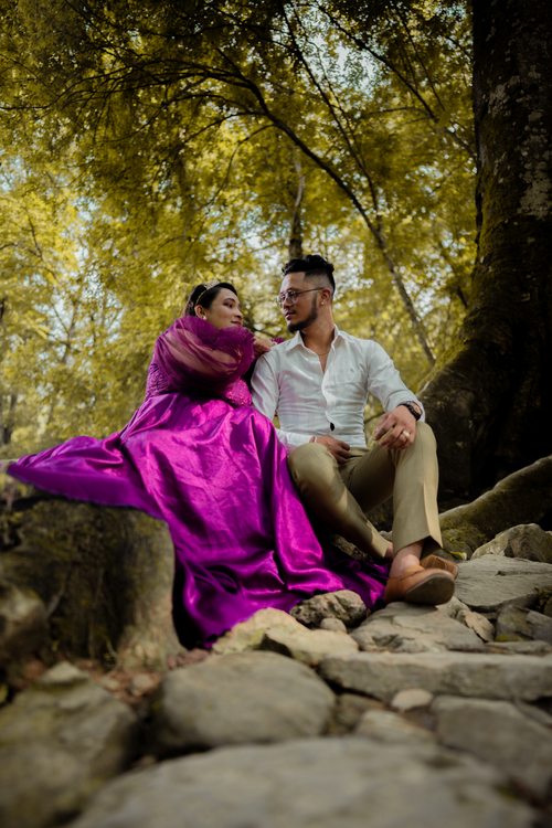 Free A couple in stylish attire sitting and posing outdoors, surrounded by lush greenery. Stock Photo