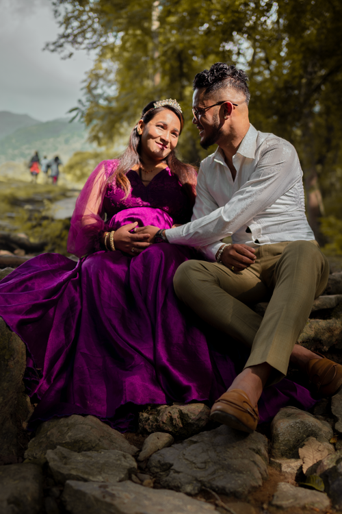 Free Expectant couple sitting on rocks in nature, expressing love and joy. Stock Photo