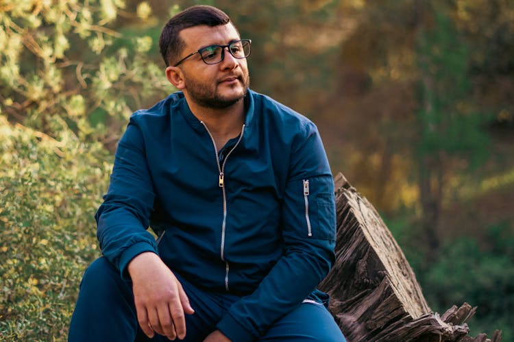 Man In Blue Tracksuit Sitting On Fell Tree Trunk