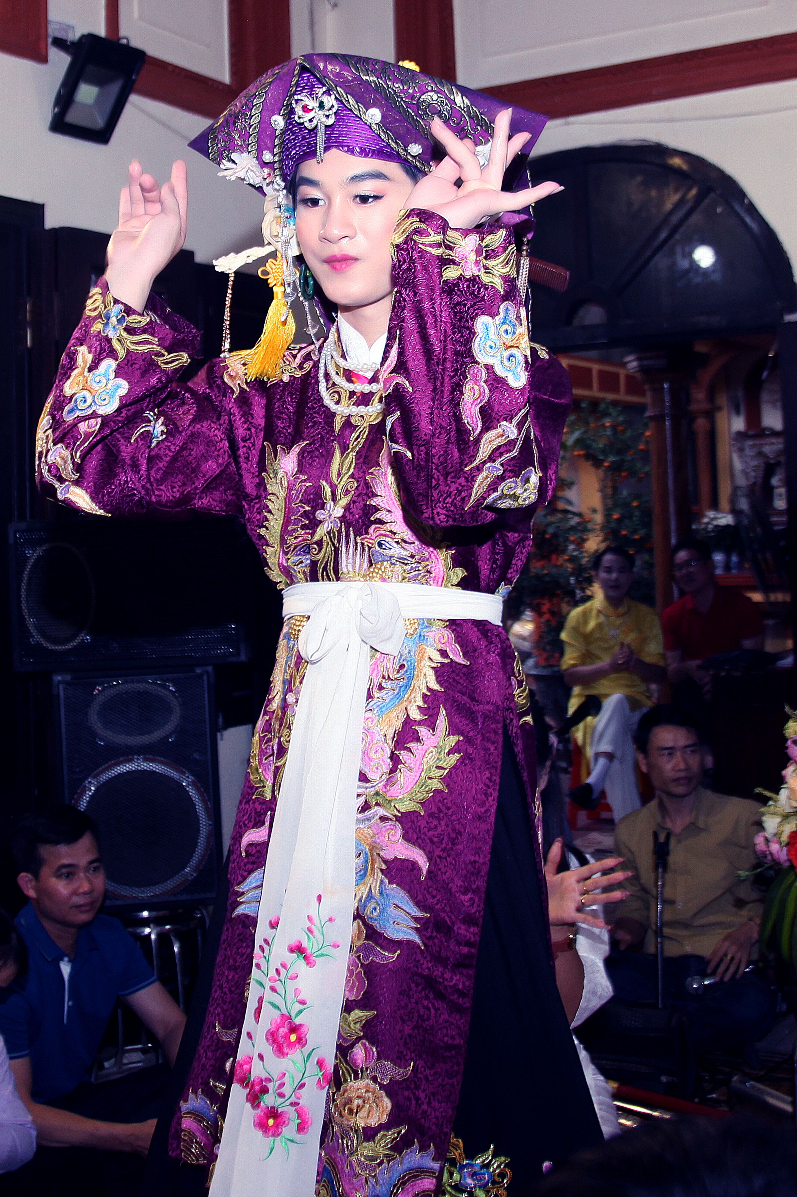 Person performing traditional dance in vibrant, ornate cultural attire during an indoor celebration.