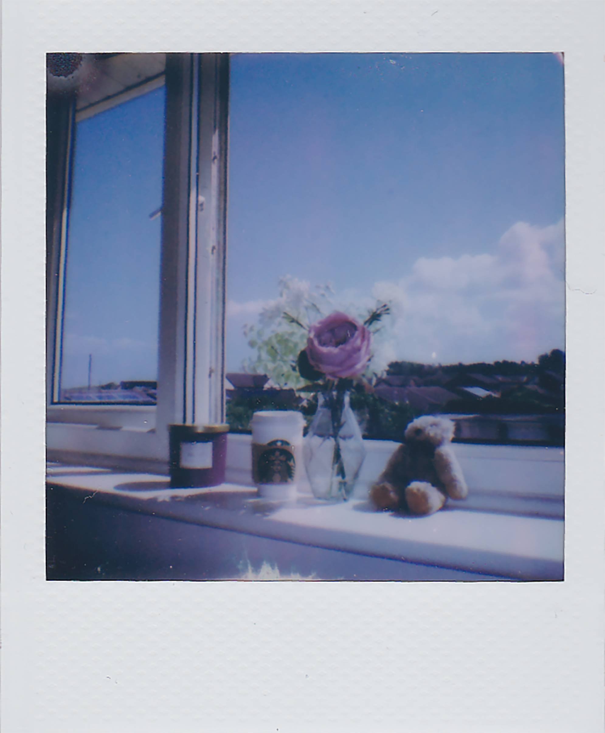 A tranquil windowsill scene featuring a vase with flowers, teddy bear, and candle under a bright blue sky.