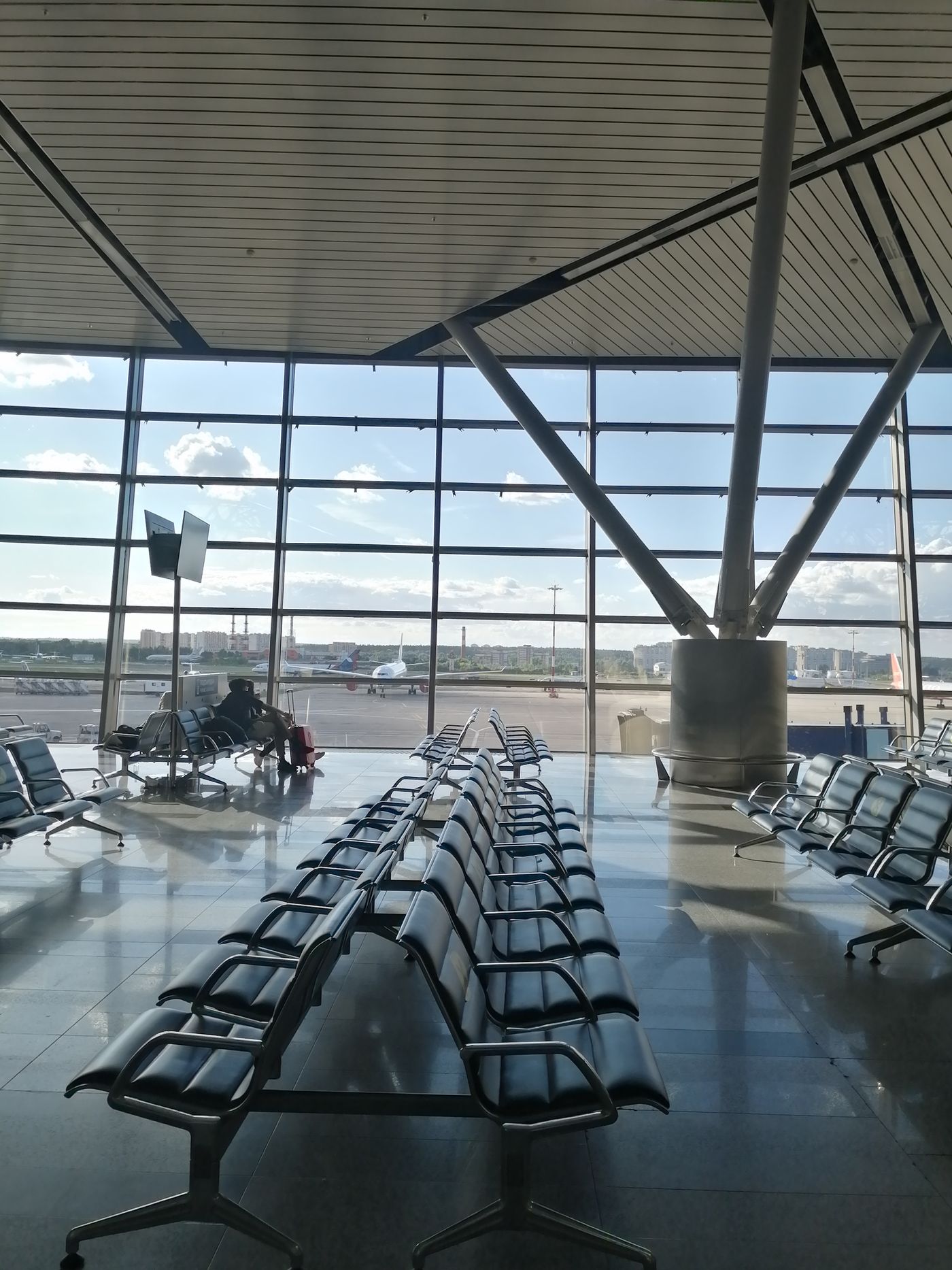 A modern airport terminal lounge with rows of seating and floor-to-ceiling windows over the runway