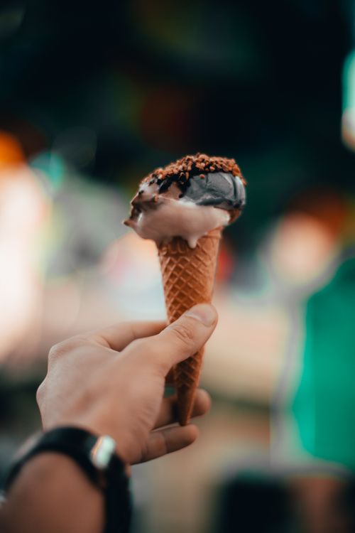 Free Close-up of a hand holding a chocolate ice cream cone with sprinkles. Soft focus and blurred background. Stock Photo