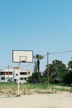 Empty basketball court under a clear blue sky, showcasing urban and natural contrast.