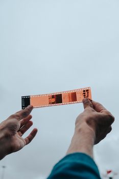 Close-up of hands holding a photographic film strip against a cloudy backdrop.