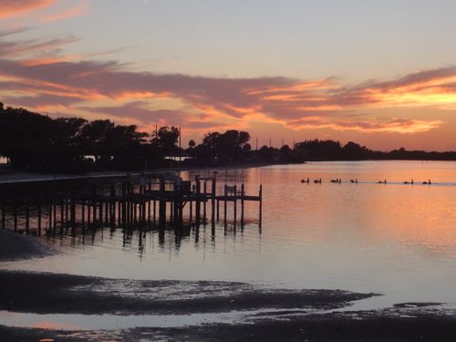 Free Enjoy a tranquil sunset view over a serene lake with a silhouetted dock and birds. Stock Photo